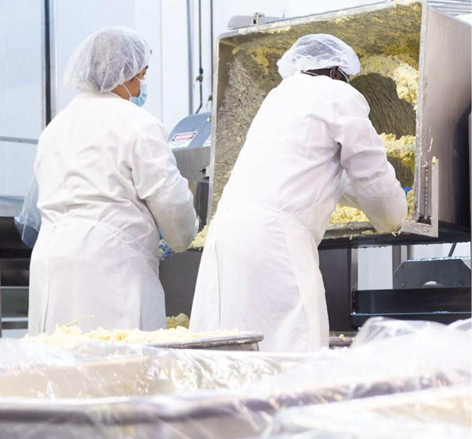 Co‑packing facility worker inspecting packaged meals in a food manufacturing line.